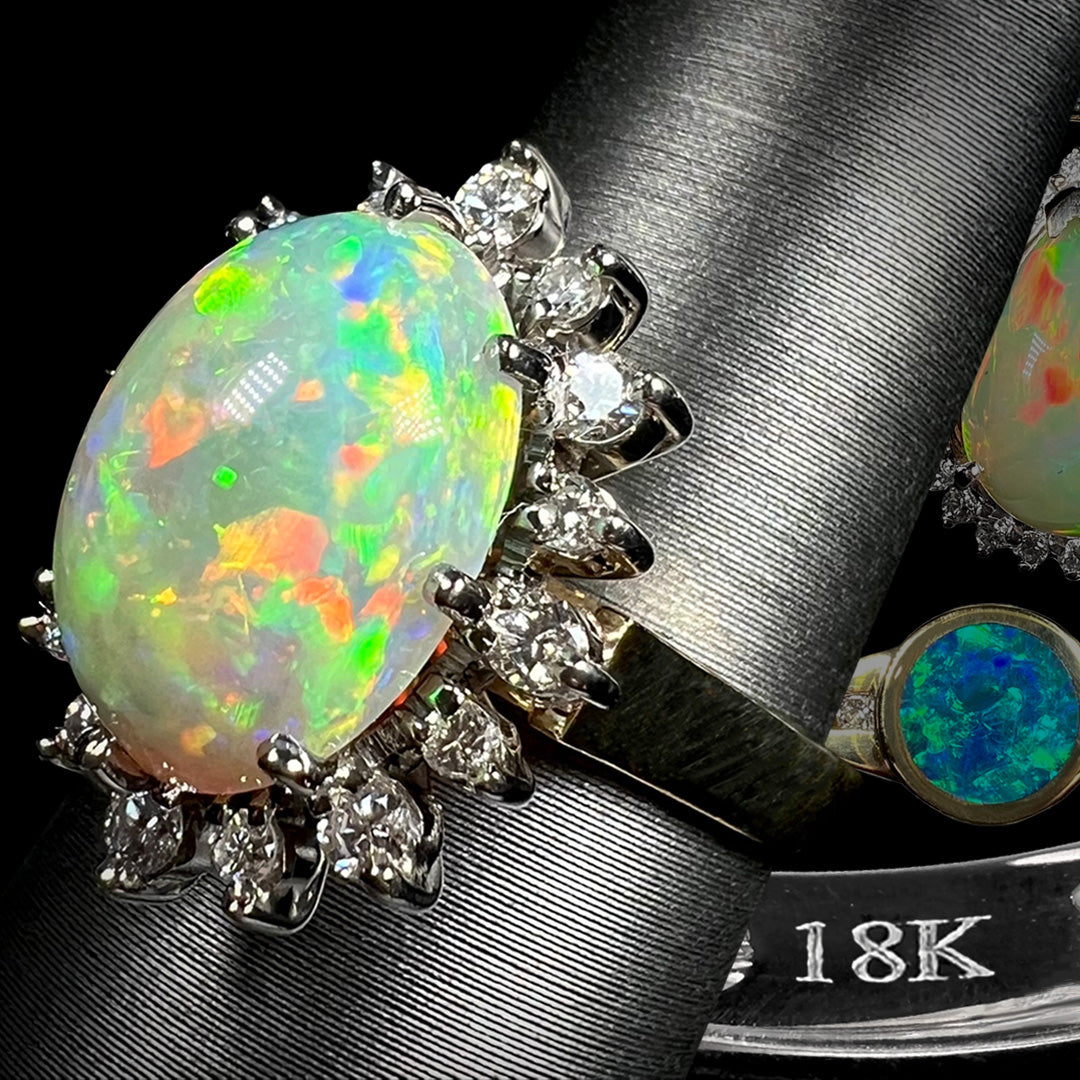 Solid 18k gold Australian fire opal and diamond ring shown on ring display from angle in front of "18K" hallmark stamp and faded gold opal rings.