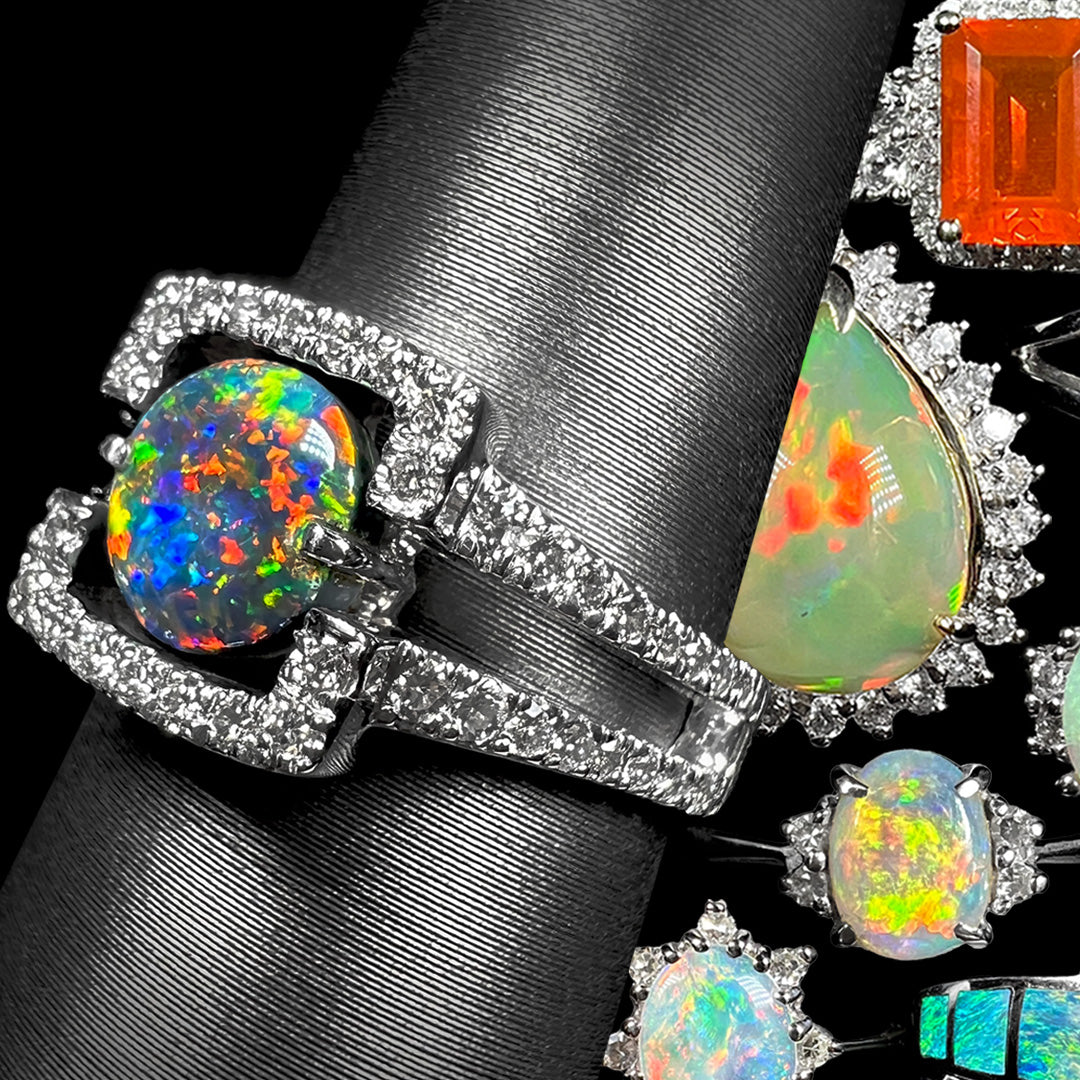 A white gold black opal and diamond ring shown on ring display from angle against background of colorful white gold opal rings.
