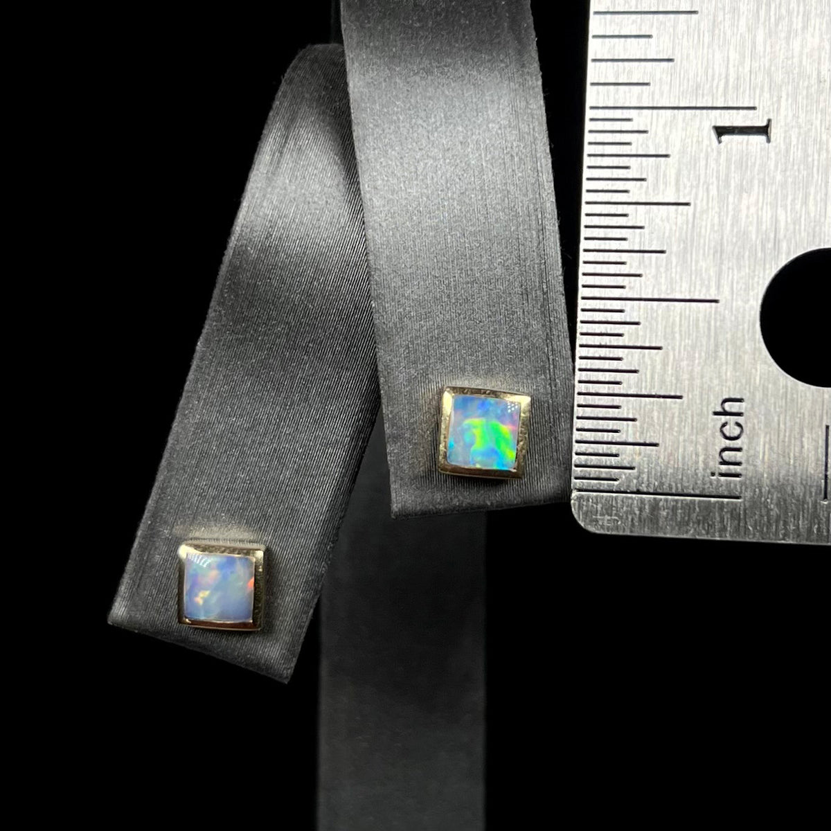 Square shaped opal stud earrings on earring display that measure 0.2 inch next to a ruler for scale