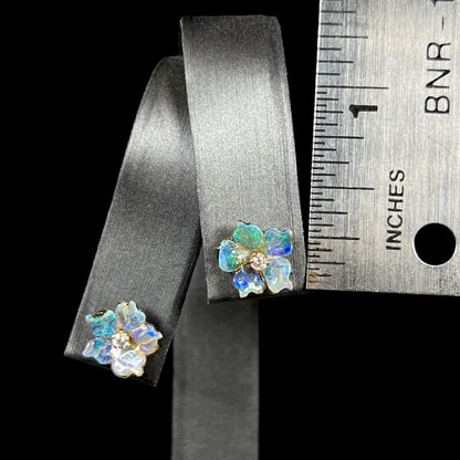 A 0.25 inch-long pair of carved boulder opal doublet flower earring jackets with gold CZ studs shown next to a ruler on an earring display.
