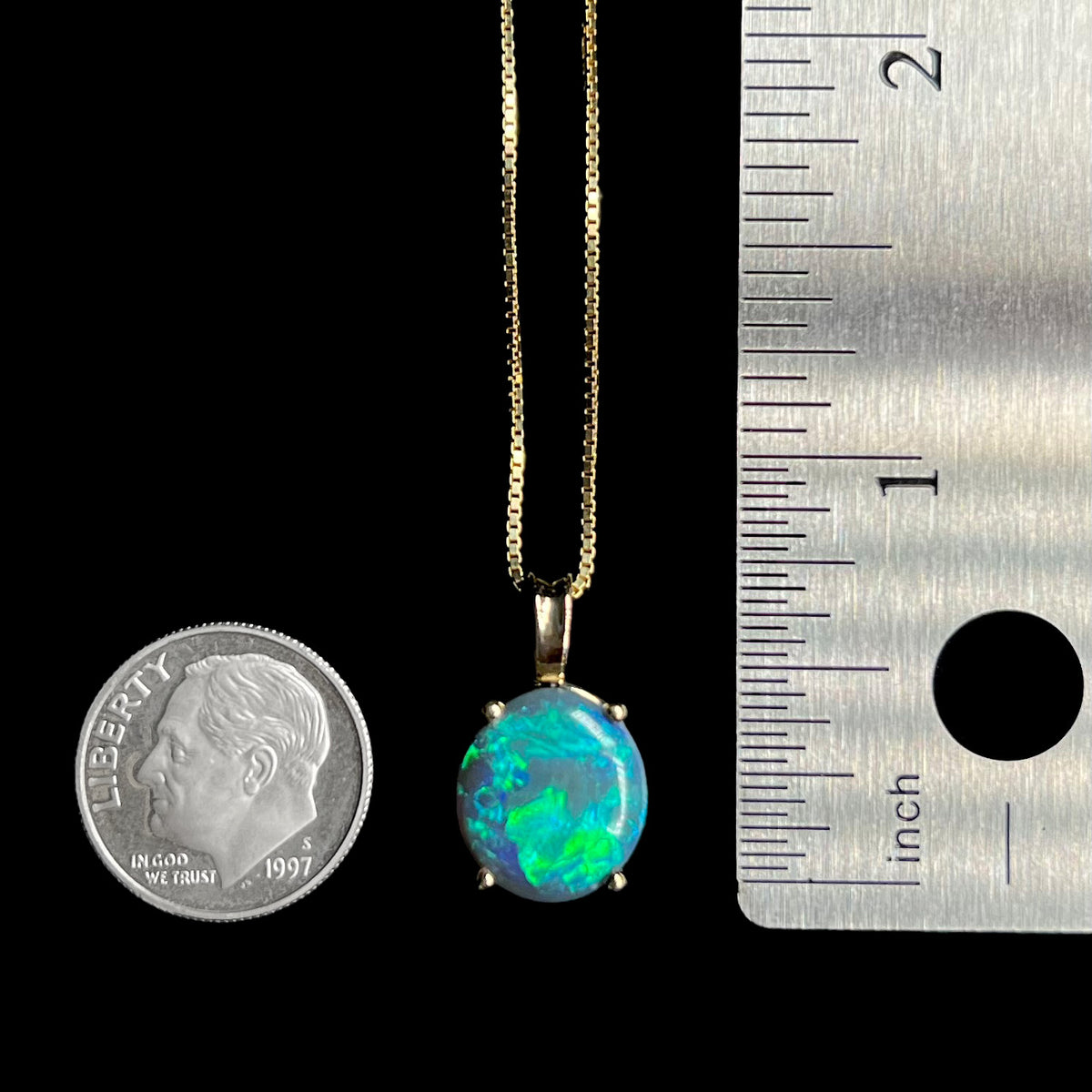 Australian black opal pendant measuring approximately 0.75 inch from the top of its gold bail, shown between US dime coin and ruler for scale