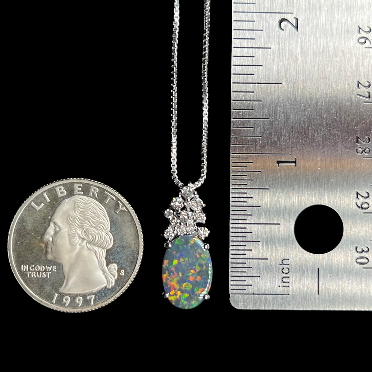 A 0.9 inch-long 2.65ct black opal and diamond pendant shown between a US quarter coin and ruler for scale.