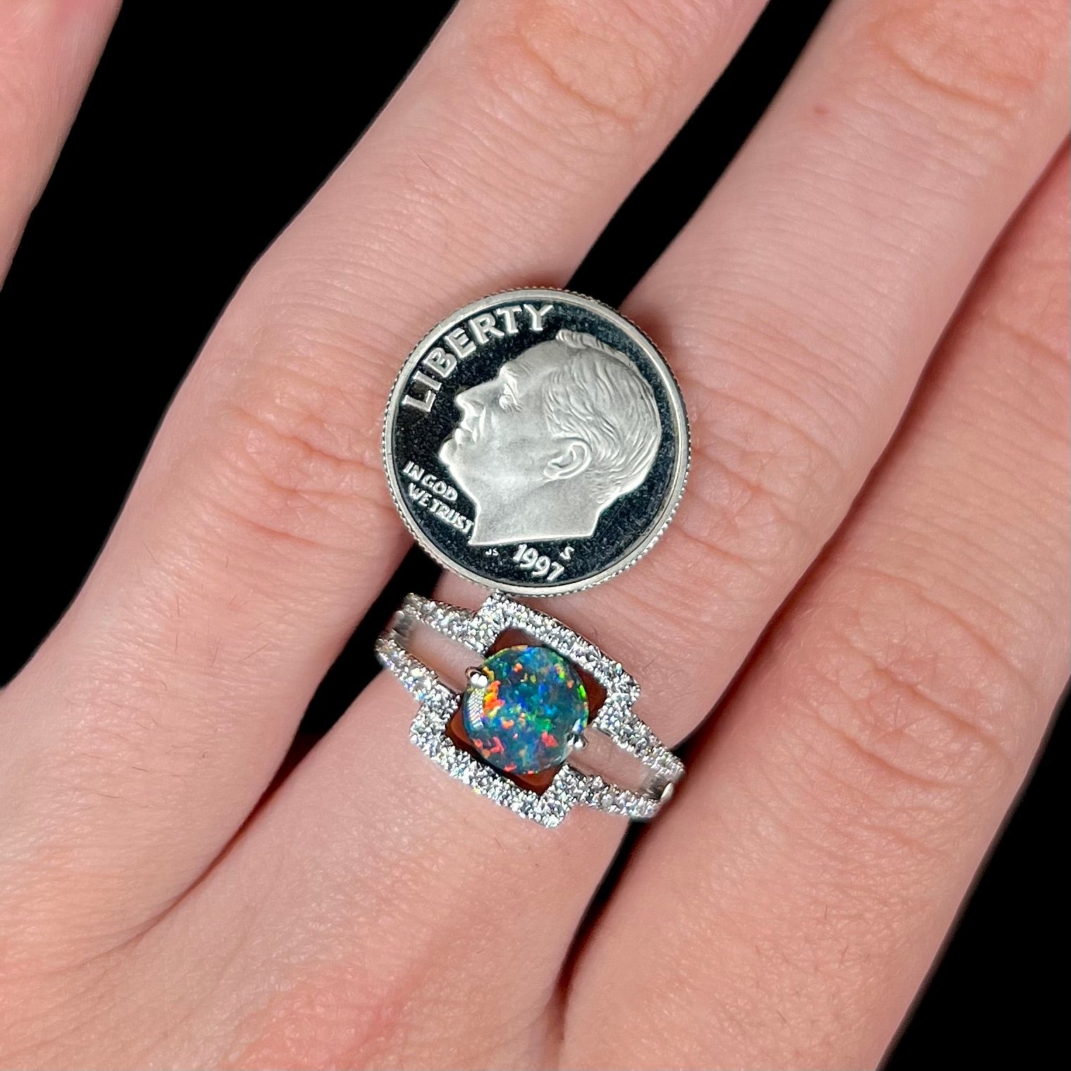 A 1.13ct black opal and diamond ring, worn on a hand next to a US dime coin.