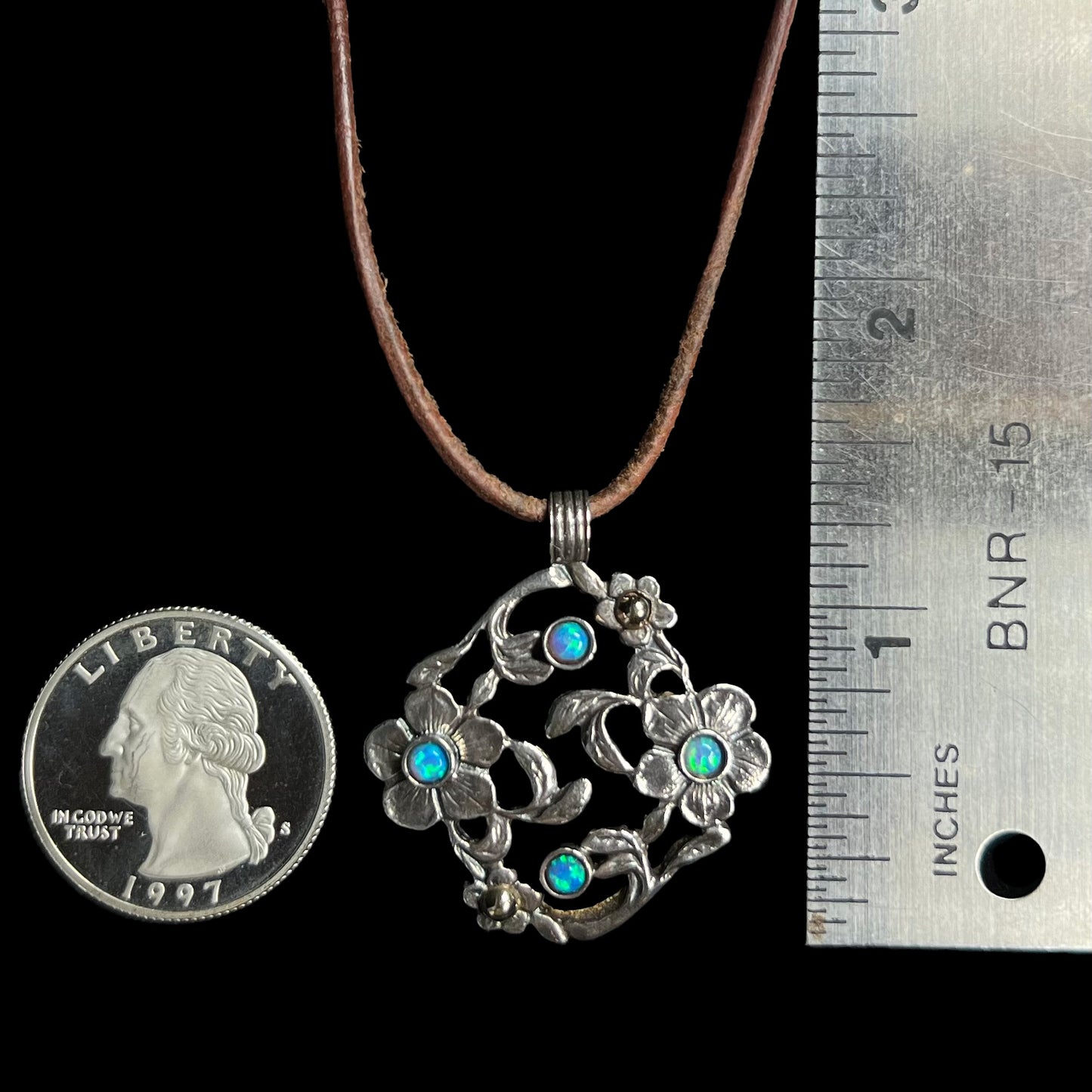 A 1.25 inch long two-tone sterling silver and 14k gold opal dogwood flower pendant next to a quarter and ruler.