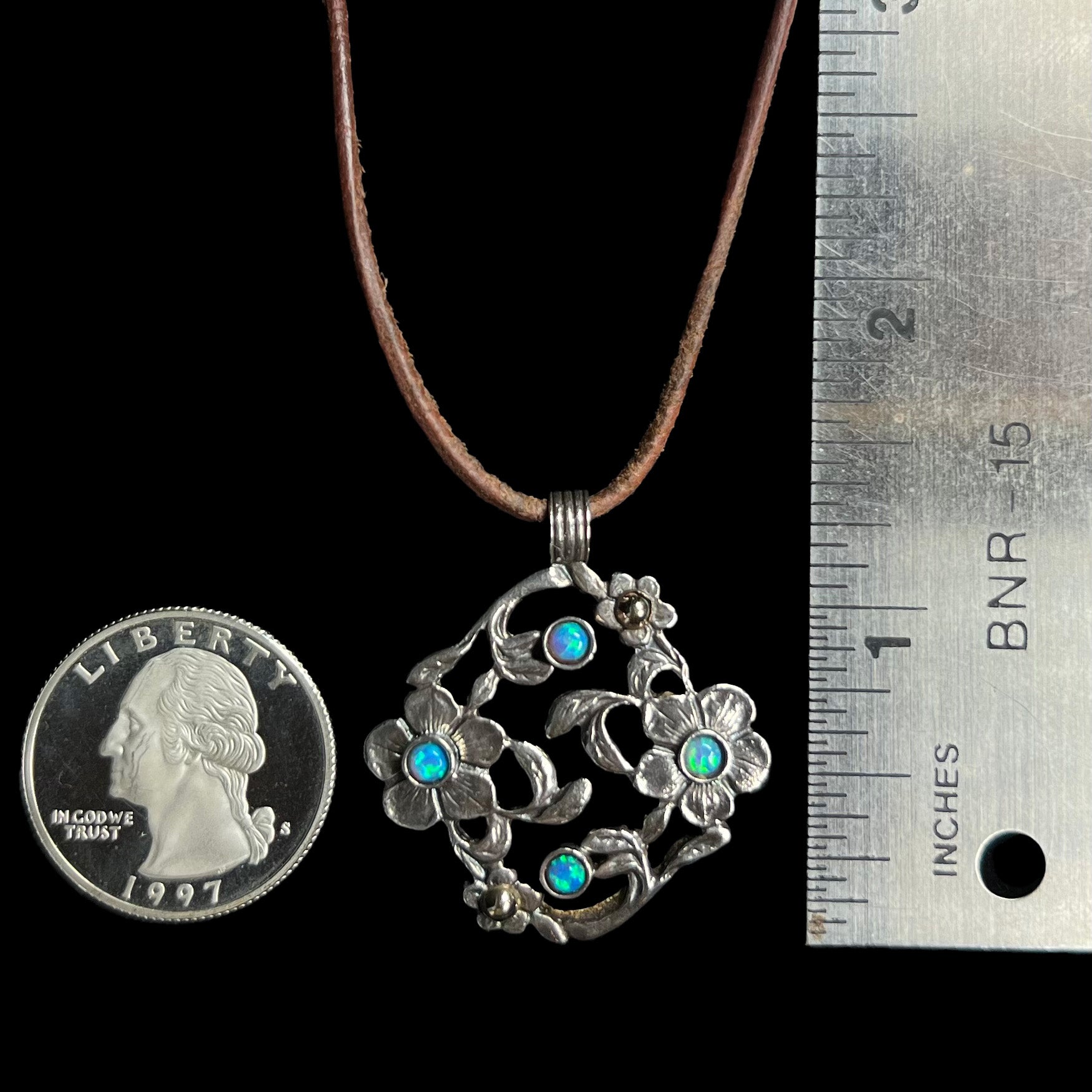 A 1.25 inch long two-tone sterling silver and 14k gold opal dogwood flower pendant next to a quarter and ruler.