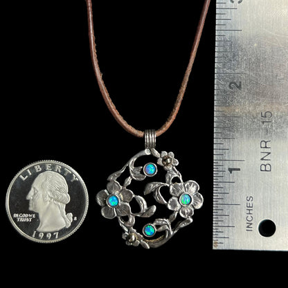 A 1.25 inch long two-tone sterling silver and 14k gold opal dogwood flower pendant next to a quarter and ruler.