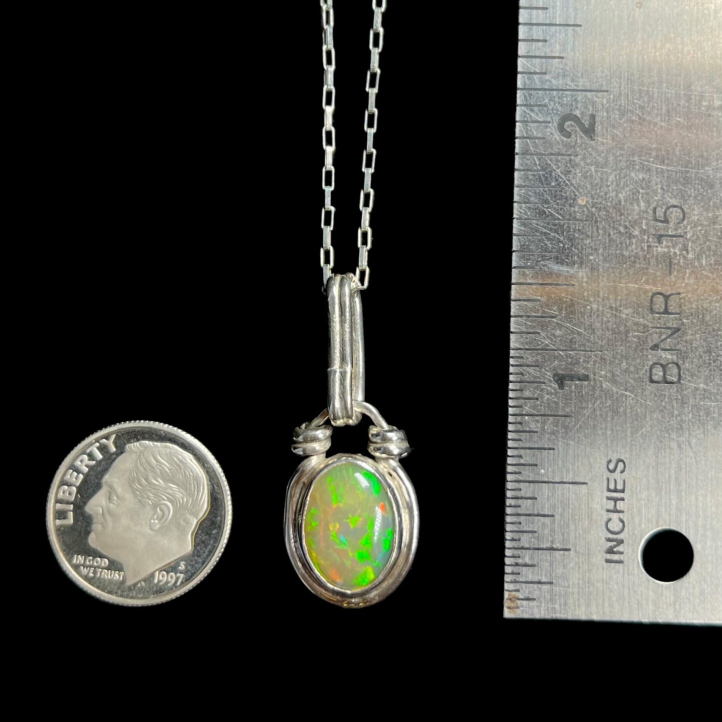A 1.25 inch long sterling silver Ethiopian opal pendant, shown next to a dime coin and ruler for scale.