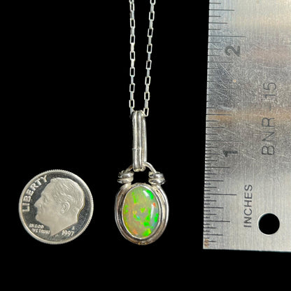 A 1.25 inch long sterling silver Ethiopian opal pendant, shown next to a dime coin and ruler for scale.
