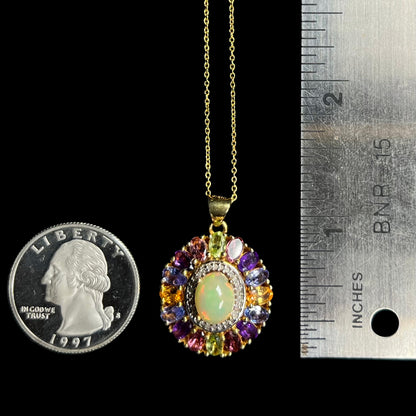 A 1.25 inch long gold plated Ethiopian opal and multi-gemstone halo pendant next to a quarter coin and ruler.