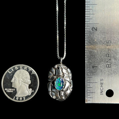 A 1.25 inch-long unisex sterling silver pinecone-inspired opal triplet pendant next to a ruler and quarter coin.