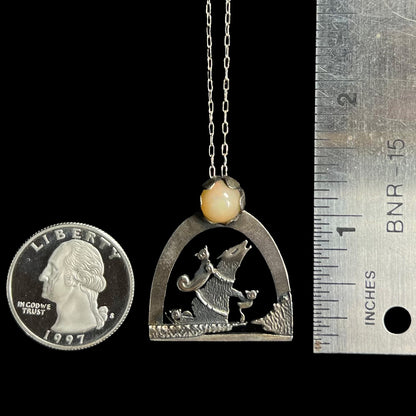 A 1.25 inch long sterling silver Ethiopian opal wolf and cat design necklace next to a quarter coin and ruler.