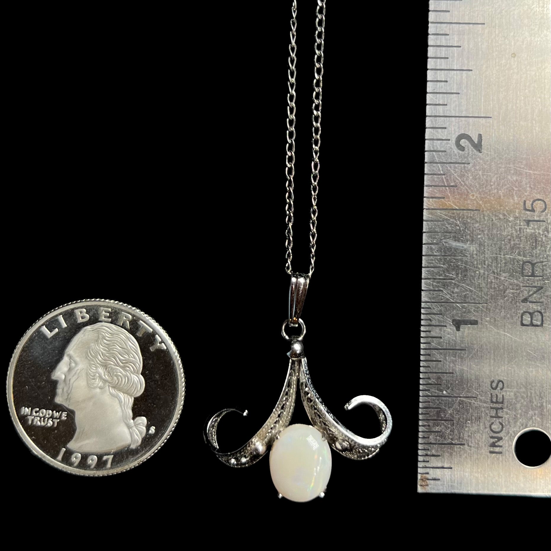 A 1.25 inch long Sorrento brand sterling silver Australian white opal pendant next to a quarter coin and ruler.