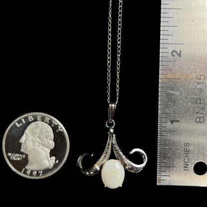 A 1.25 inch long Sorrento brand sterling silver Australian white opal pendant next to a quarter coin and ruler.