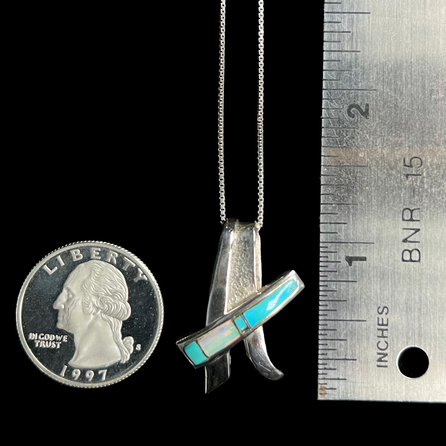 A folded design sterling silver turquoise and lab-created opal inlay necklace shown next to a quarter and ruler.