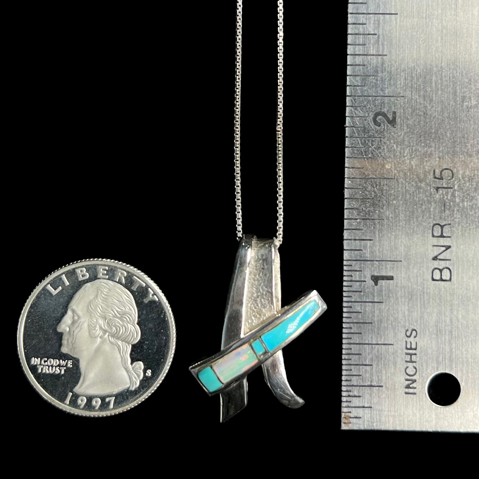 A folded design sterling silver turquoise and lab-created opal inlay necklace shown next to a quarter and ruler.