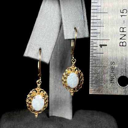 1.33 inch-long vintage yellow gold Australian light opal dangle earrings shown on an earring display next to a ruler.