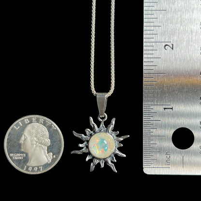 A 1.33 inch-long sterling silver sun pendant set with an imitation opal, shown next to a US quarter coin and ruler for scale.