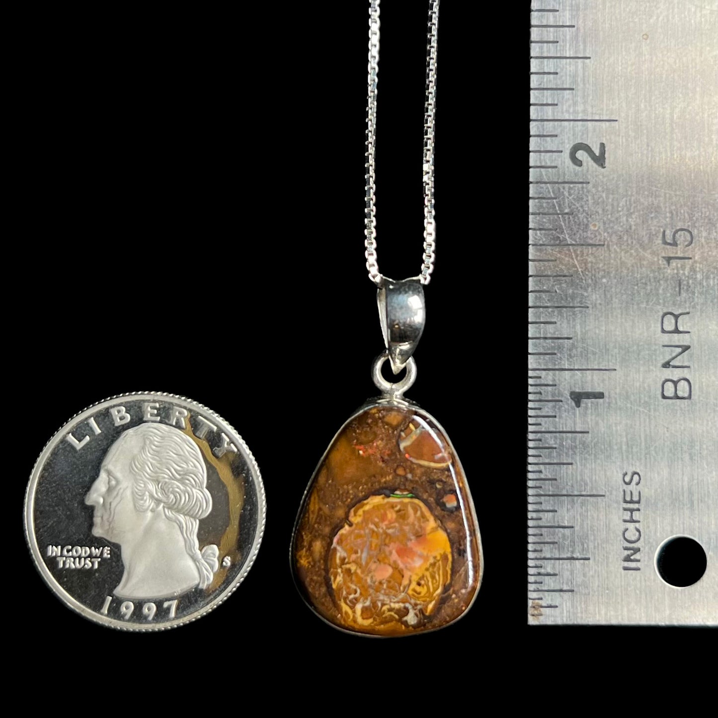 A 1.33 inch long Yowah nut boulder opal pendant in sterling silver, shown next to a ruler and 1997 S US quarter coin.