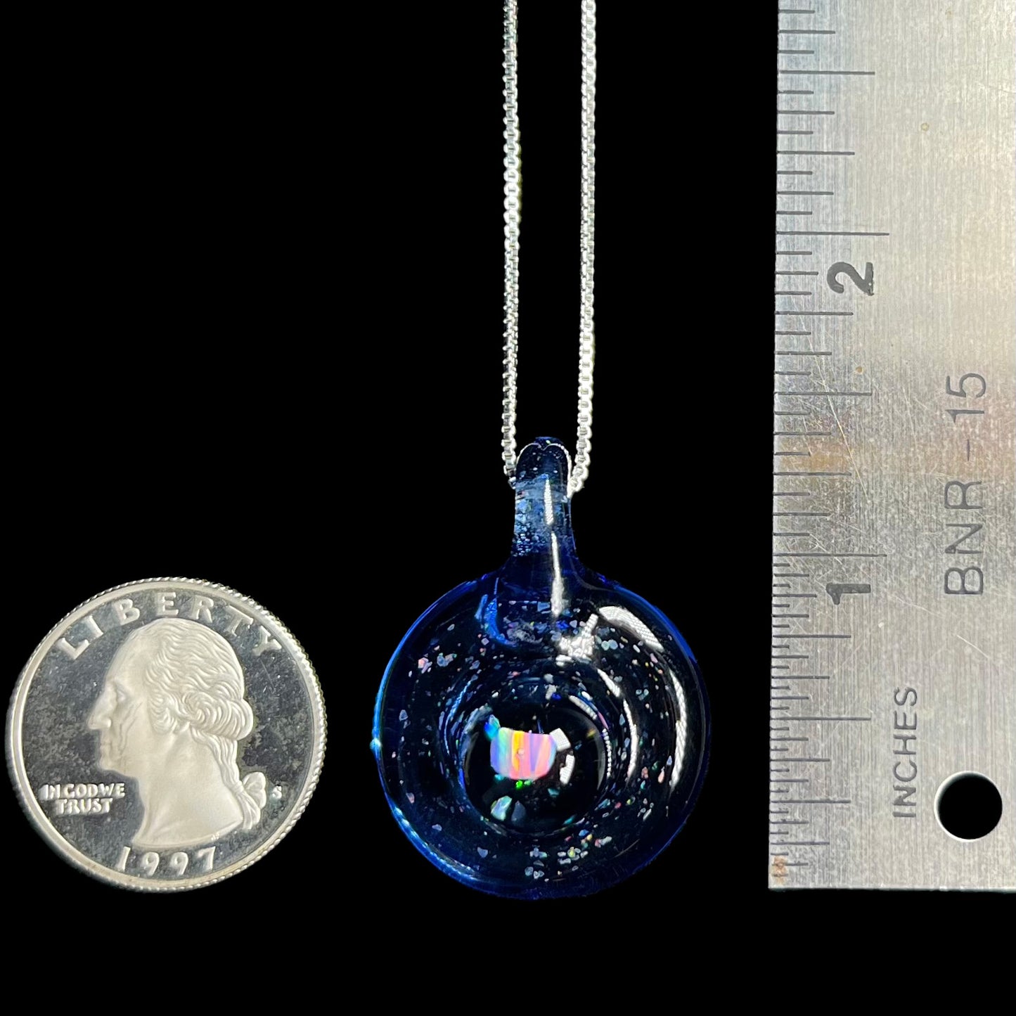 A 1.4 inch-long lab-created opal in glass pendant shown next to a ruler and a US quarter coin for scale.