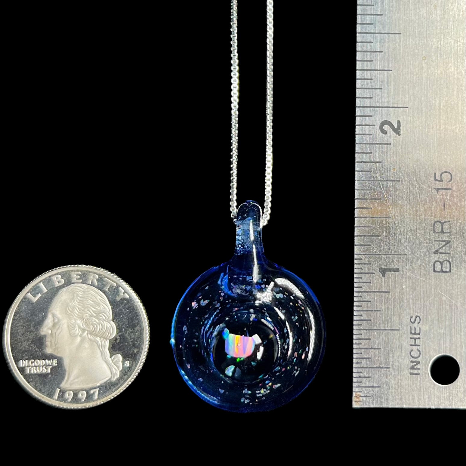 A 1.4 inch-long lab-created opal in glass pendant shown next to a ruler and a US quarter coin for scale.