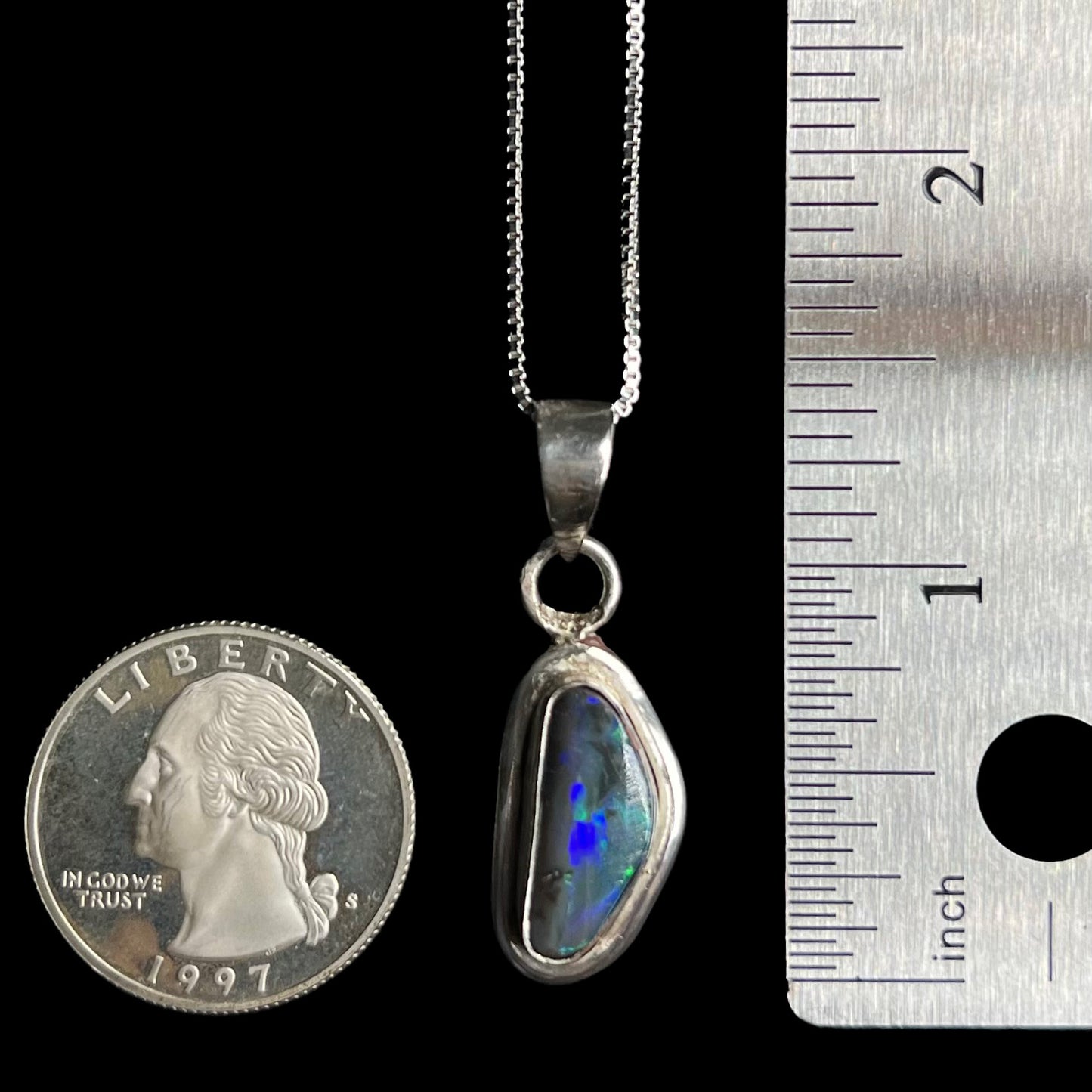 A 1.4 inch-long sterling silver black opal pendant on a chain shown next to US quarter coin and ruler for scale.