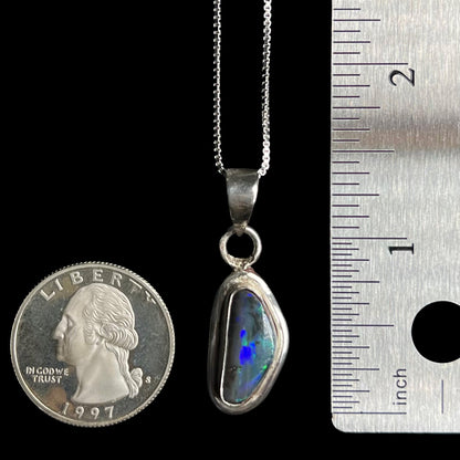 A 1.4 inch-long sterling silver black opal pendant on a chain shown next to US quarter coin and ruler for scale.