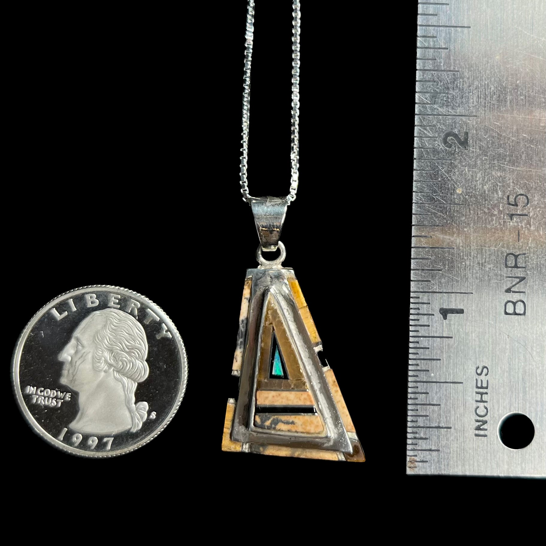 A 1.5 inch long sterling silver opal, picture jasper, and onyx inlay pendant shown next to a quarter and ruler.