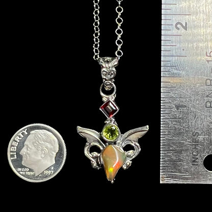 A 1.5 inch long silver opal angel pendant shown next to a ruler and dime coin.