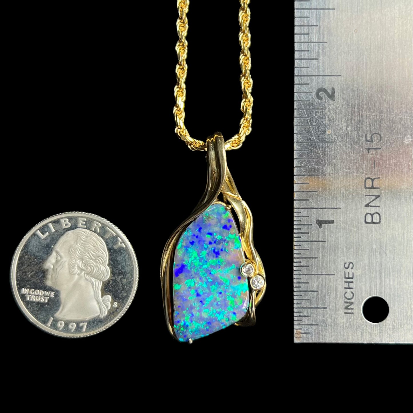 1.6 inch-long yellow gold boulder opal and diamond pendant next to a ruler and US quarter coin for scale.