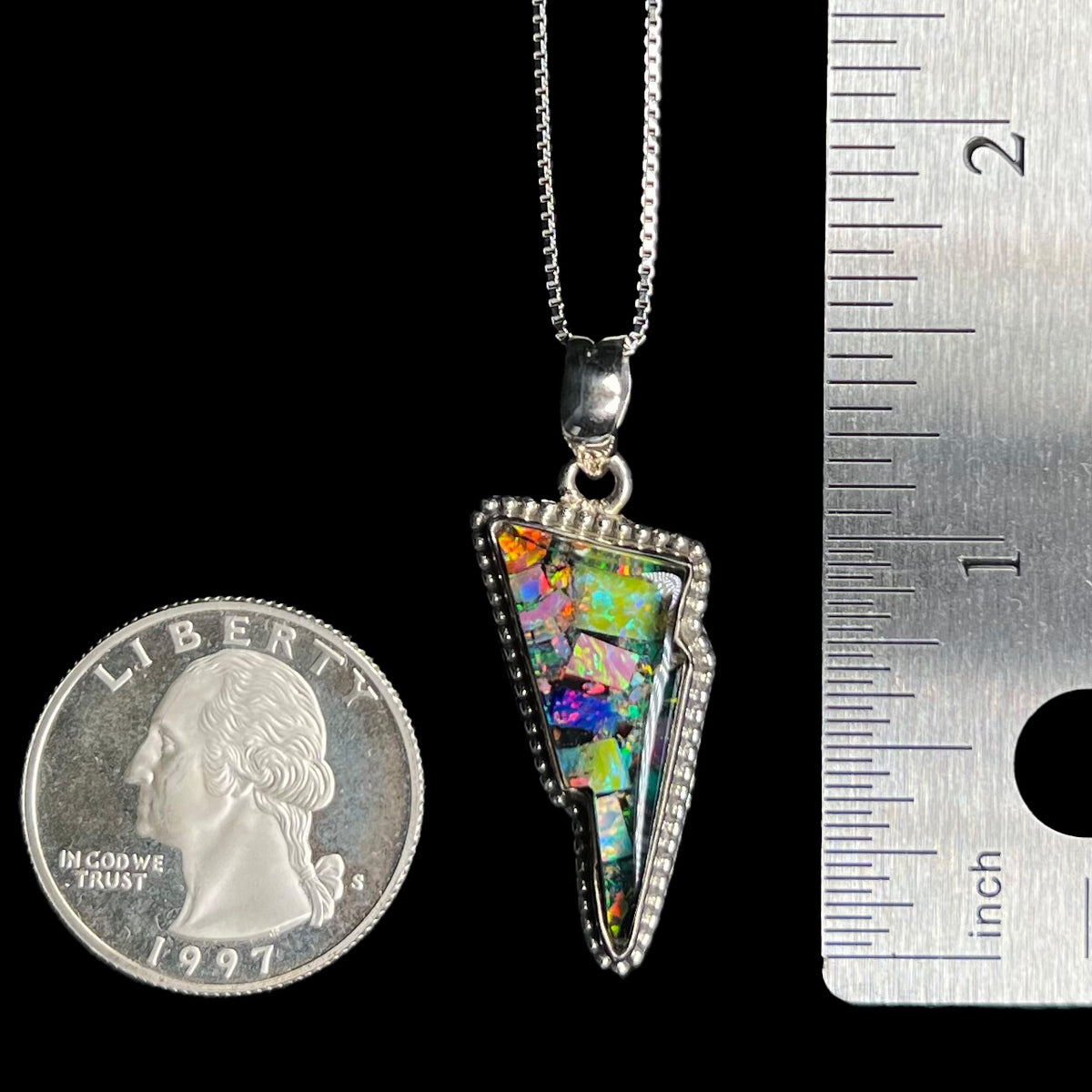 Close-up of 1.6 inch-long sterling silver lightning bolt pendant set with mosaic opal, shown on box chain between US quarter coin and ruler.