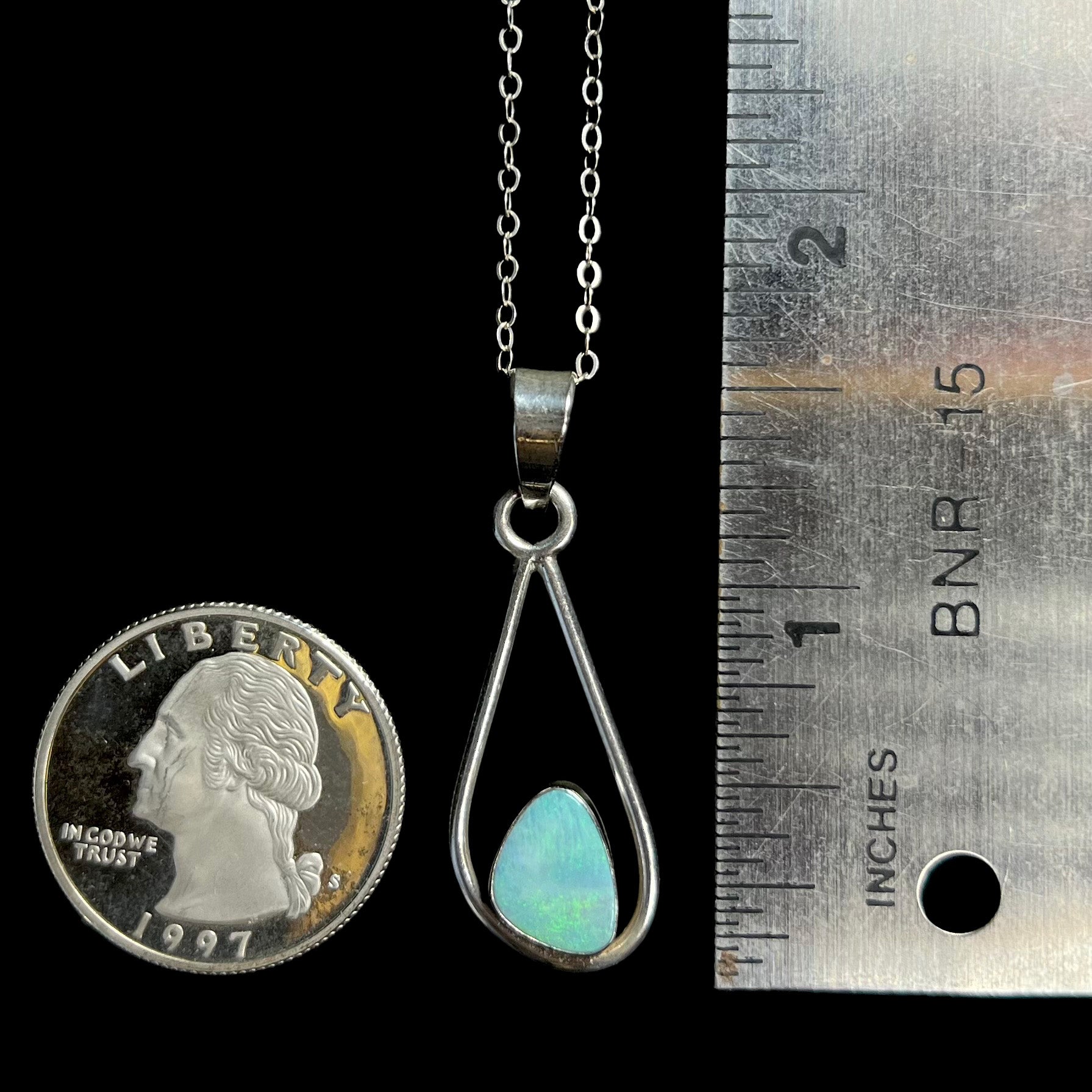 A 1.6 inch-long sterling silver opal doublet pendant shown on a black background next to a ruler and US quarter coin.