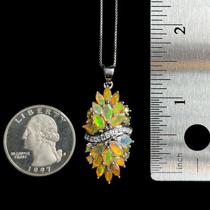 A 1.6 inch-long women's Ethiopian fire opal pendant on a sterling silver chain between a US quarter coin and a ruler.