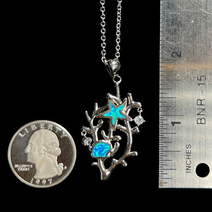A 1.75 inch long silver plated coral reef necklace with lab-created opal inlay next to a ruler and quarter.