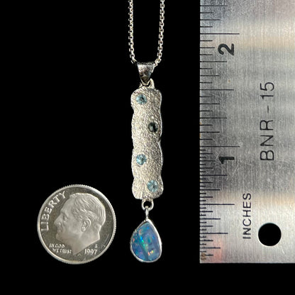 A 1.75 inch-long sterling silver dangling opal doublet drop pendant shown next to a ruler and US dime coin for scale.