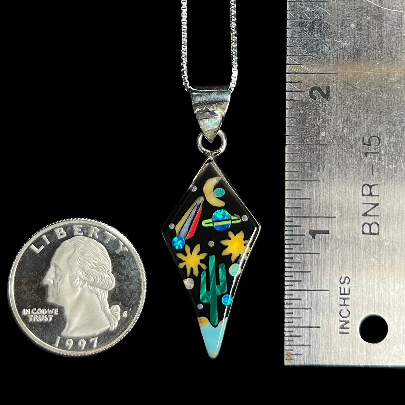 1.9 inch-long silver inlay pendant with desert and space motif next to ruler and US quarter.