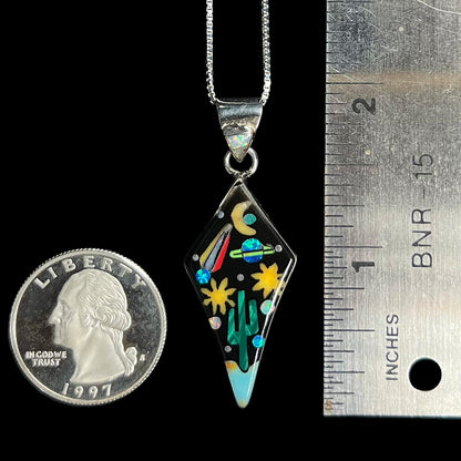 1.9 inch-long silver inlay pendant with desert and space motif next to ruler and US quarter.