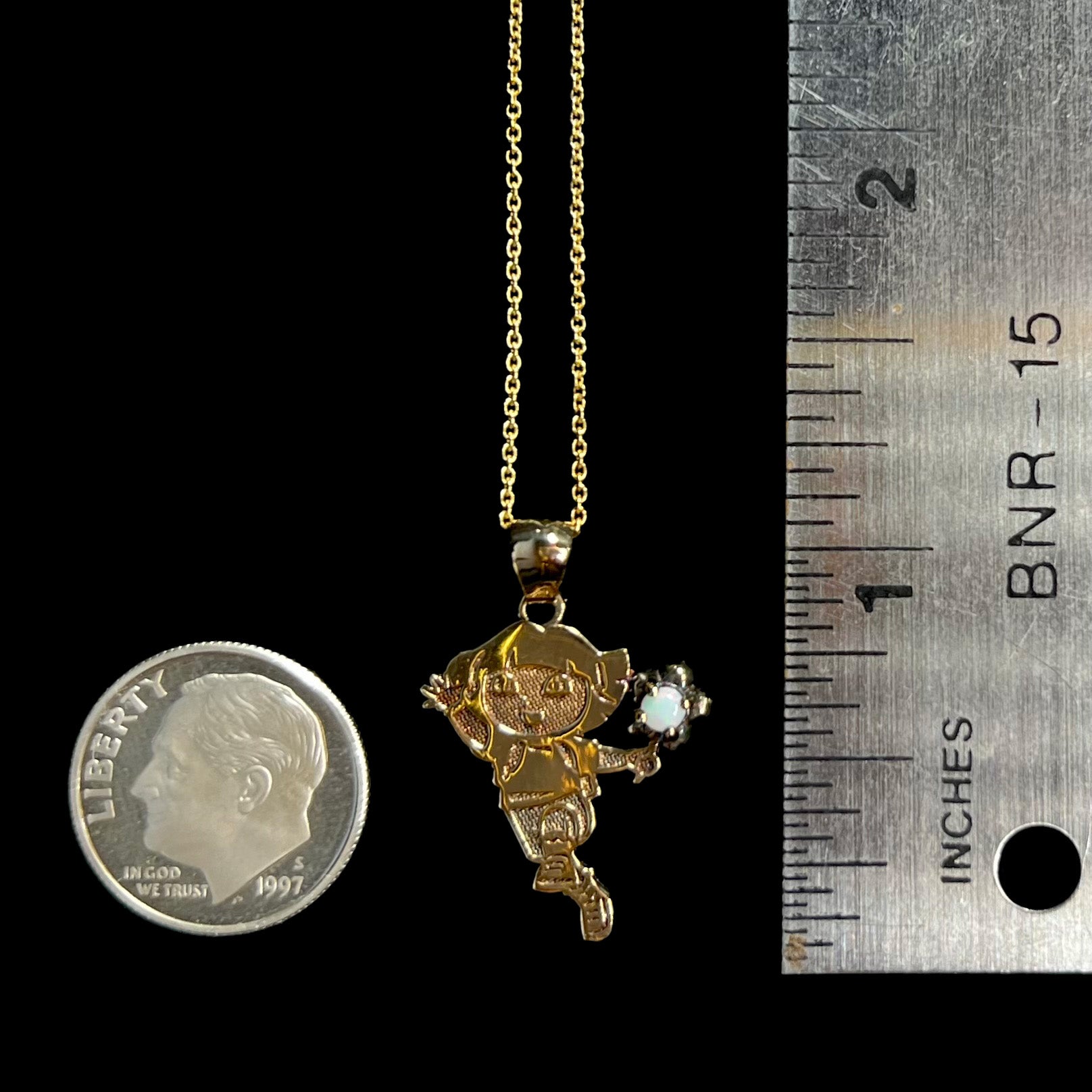1 inch-long Dora the Explorer opal pendant shown on a black background next to a ruler and US dime coin.
