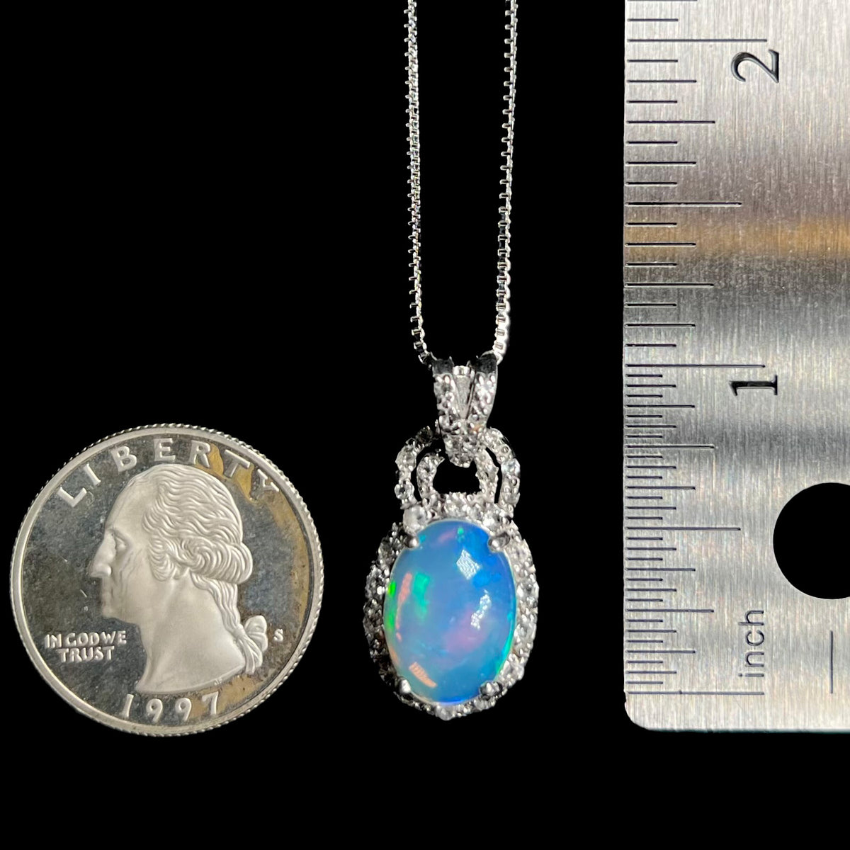 1 inch-long sterling silver Ethiopian opal pendant with topaz halo, shown between US quarter coin and ruler