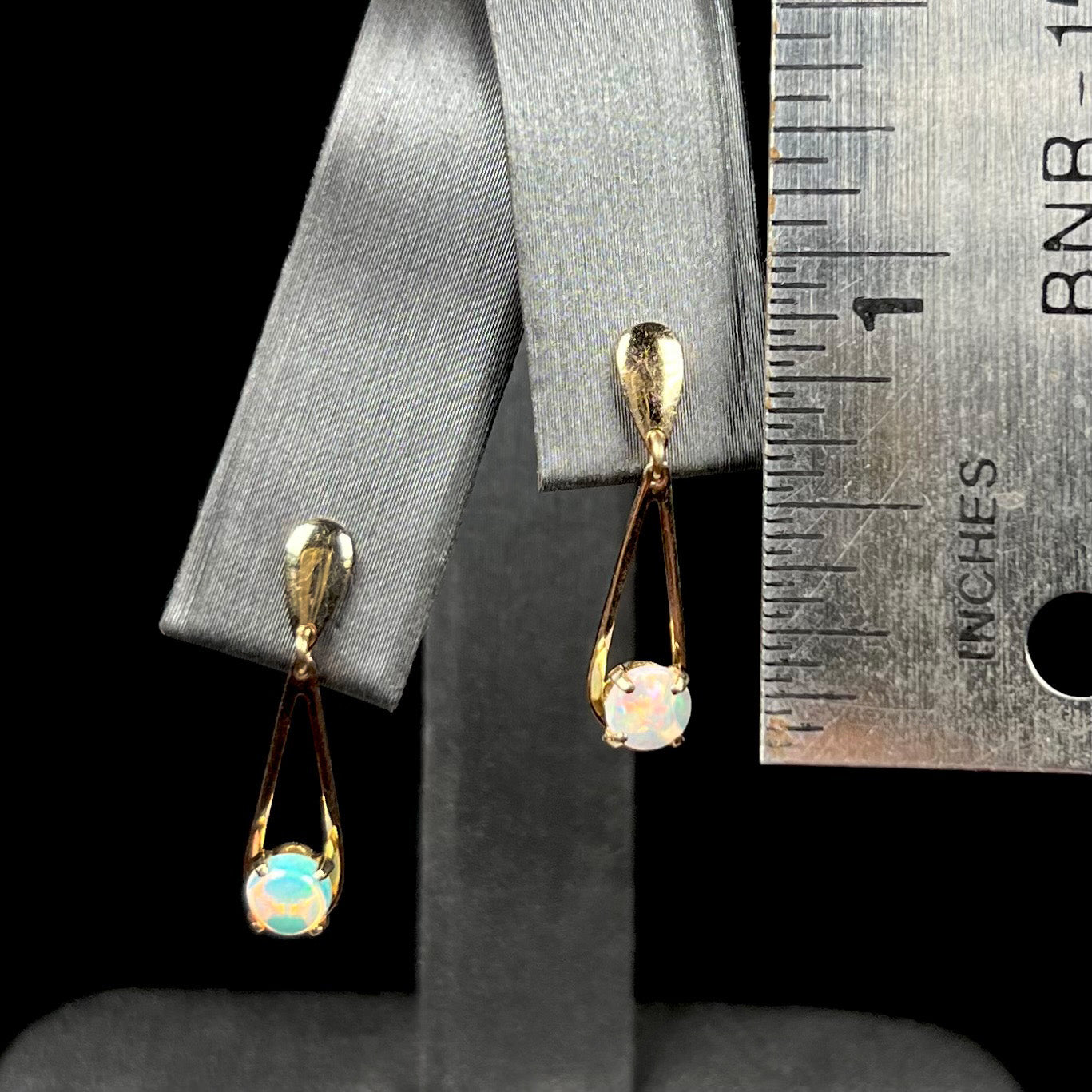1 inch-long gold opal drop earrings on earring display next to ruler.