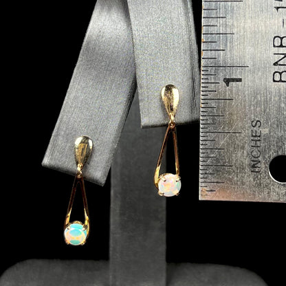 1 inch-long gold opal drop earrings on earring display next to ruler.