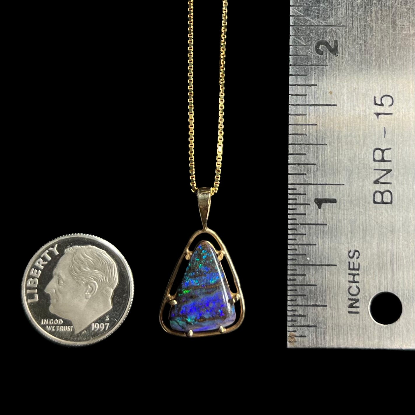 A 1 inch long Duck Creek opalized wood pendant in 9k gold, shown next to a ruler and dime coin.
