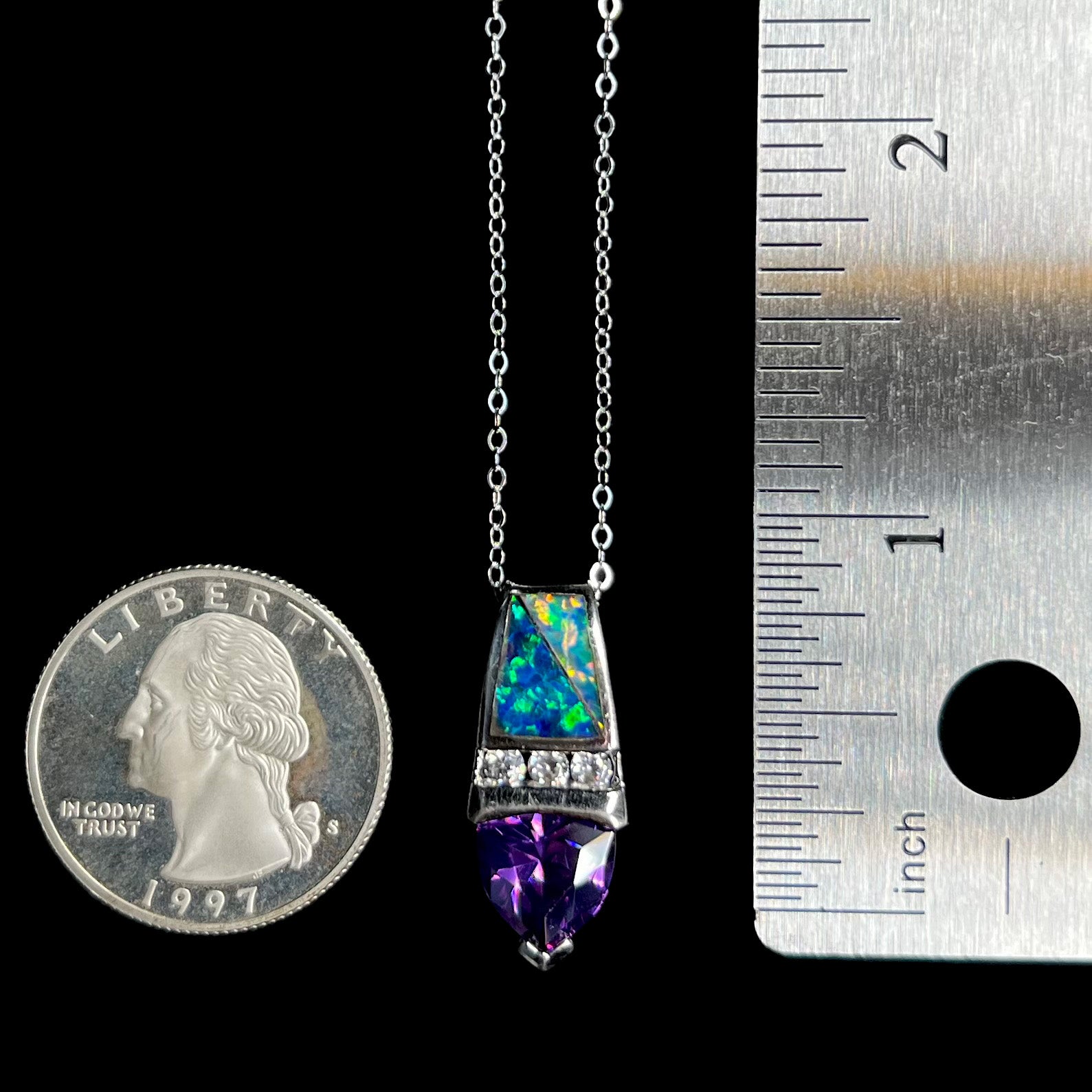 A 1 inch-long sterling silver opal inlay and purple CZ drop pendant on a silver cable chain between a US quarter coin and ruler for scale.