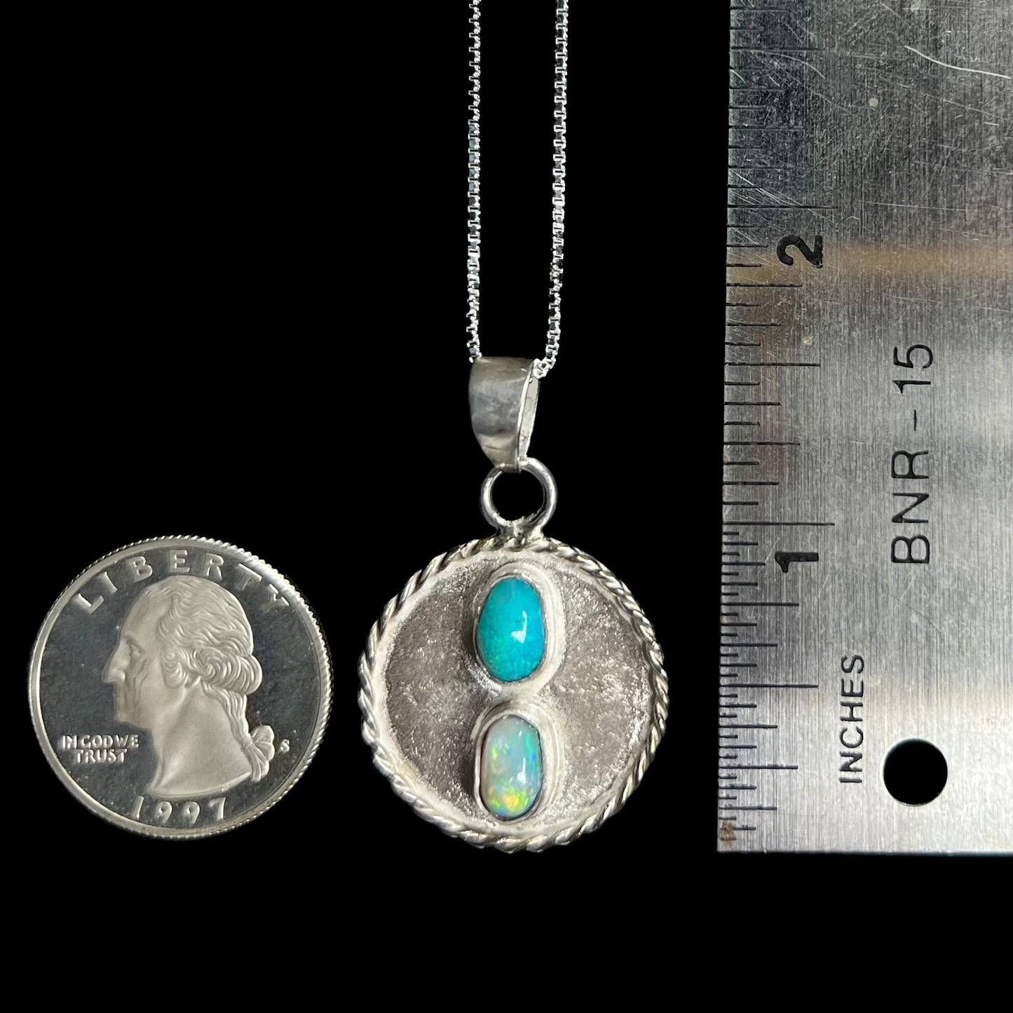 A men's sterling silver two-stone opal medallion pendant that measures 1 inch in diameter is shown next to a ruler and US quarter coin for scale.