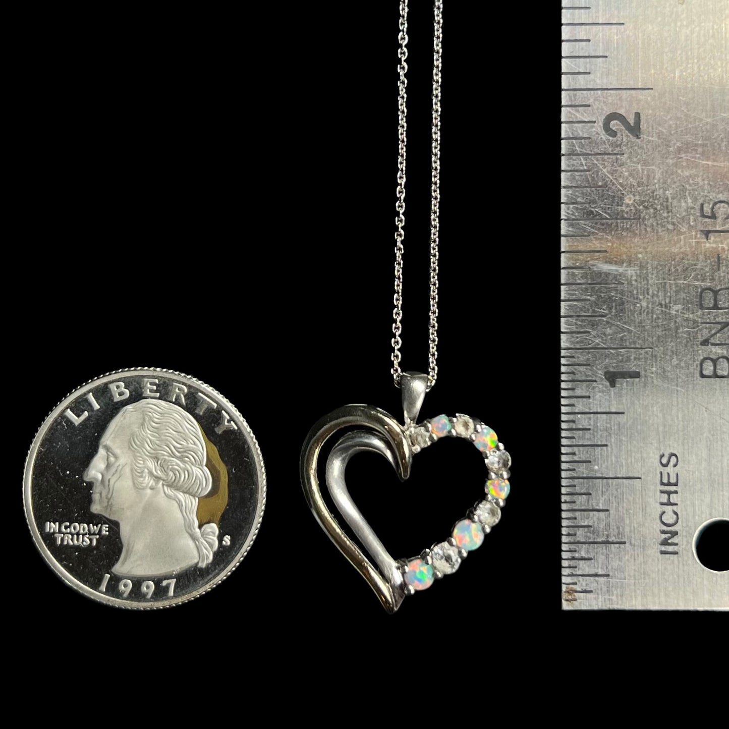 A 1 inch long sterling silver and gold opal and CZ heart necklace next to a quarter coin and ruler.