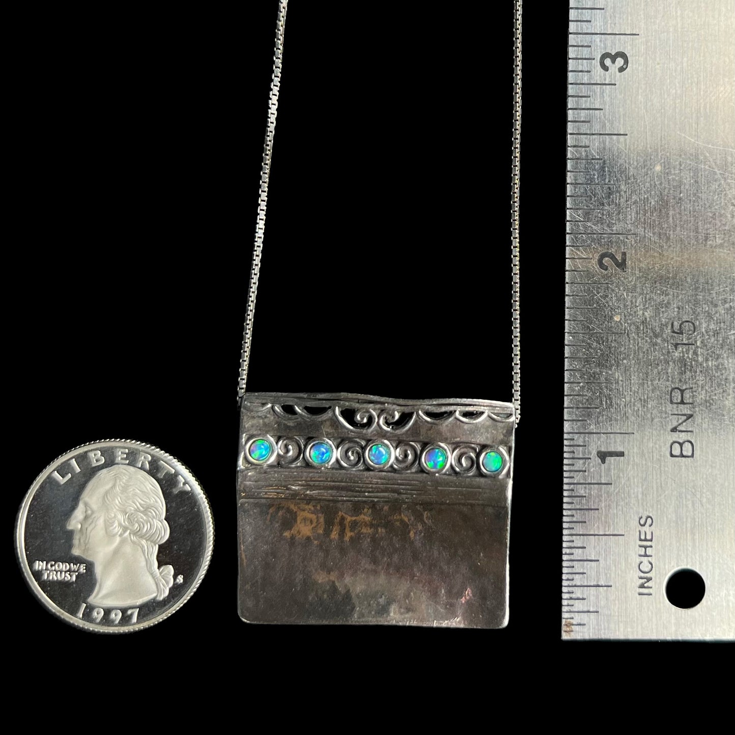 A 1 inch long Israeli sterling silver opal necklace with a hammered finish, next to a ruler and quarter coin.