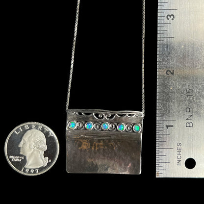 A 1 inch long Israeli sterling silver opal necklace with a hammered finish, next to a ruler and quarter coin.