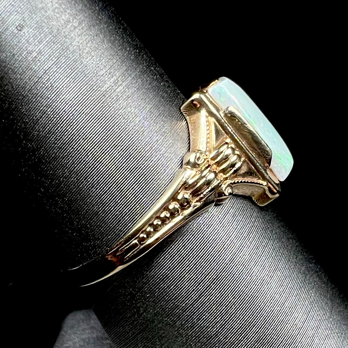 Side shank view of a 10k gold Art Deco opal solitaire ring on a ring display