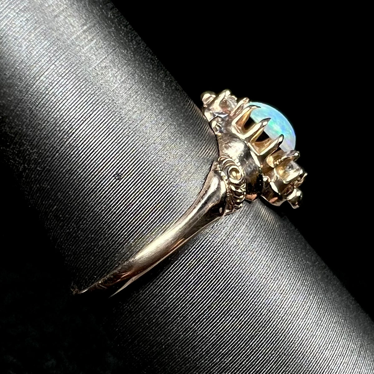 Side view of a 10k gold opal ring with Art Nouveau design on a ring display; the ring's shank is in focus, as is a rose motif on the ring's shoulder