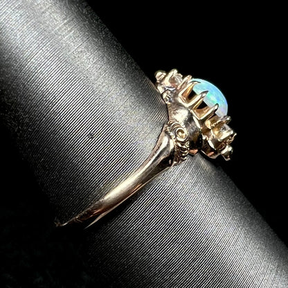 Side view of a 10k gold opal ring with Art Nouveau design on a ring display; the ring's shank is in focus, as is a rose motif on the ring's shoulder