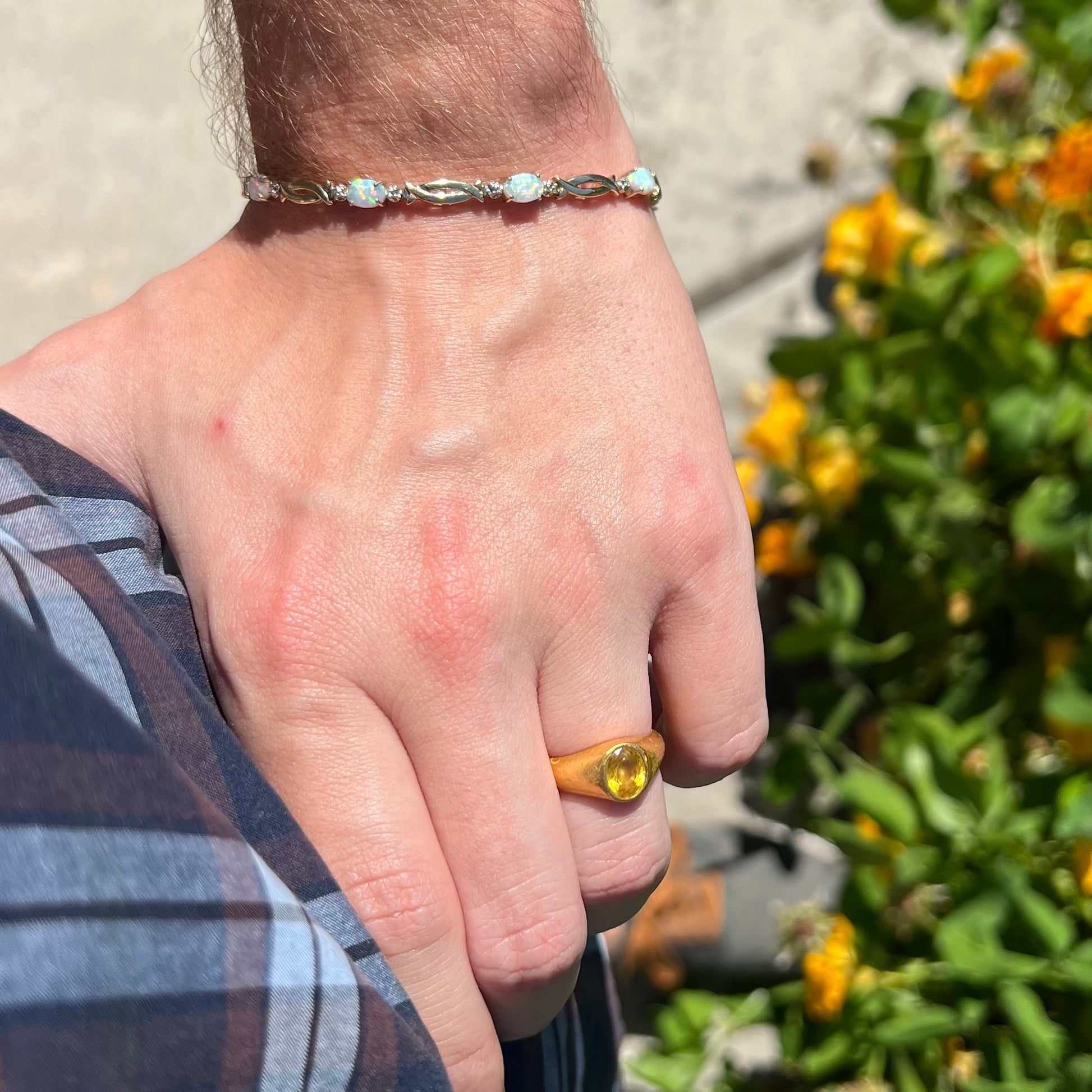 Hand resting on person's hip while wearing 24k gold ring on finger and 10k gold lab-created opal bracelet on wrist in sunlight.